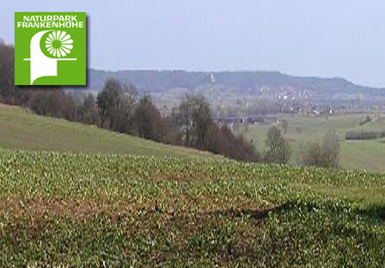 Blick über die Landschaft des Naturparks Frankenhöhe mit Feldern und Wiesen, Logo Naturpark Frankenhöhe